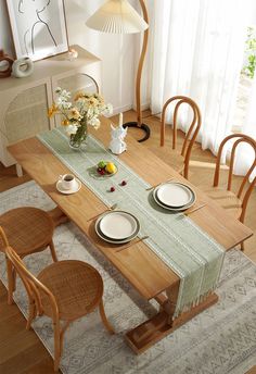 a dining room table with place settings and plates on it, in front of a window