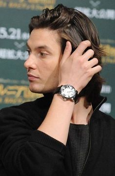 a man holding his hand up to his ear while wearing a black jacket and watch