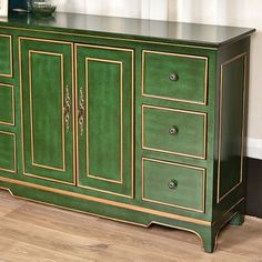 a green cabinet with gold trim on the doors and drawers is in front of a window