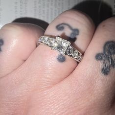 a person has tattoos on their fingers and is wearing a wedding ring with three stones