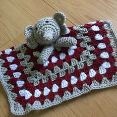 a crocheted teddy bear laying on top of a red and white afghan blanket