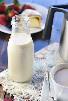 a glass bottle of milk next to a cup of coffee on a table with strawberries