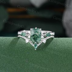 a green and white diamond ring on top of a green velvet covered surface with other jewelry items in the background