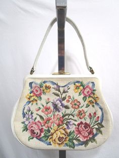 a white purse with flowers on it is hanging from a metal hook and has a long handle