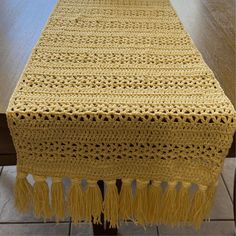 a yellow crocheted table runner with tassels on the end and bottom