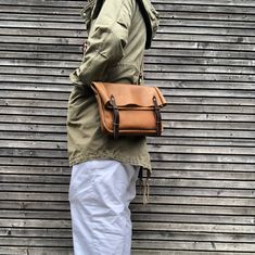 a person with a brown bag standing in front of a metal wall wearing white pants