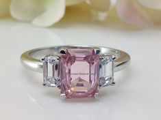 a pink and white diamond ring sitting on top of a table next to some flowers