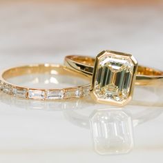 two yellow gold engagement rings with an emerald and baguette cut diamond in the middle