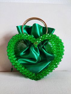 a green handbag with a ring handle and beaded decoration on the front, sitting on a white surface