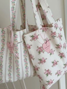 two white bags with pink flowers on them hanging from the wall next to each other