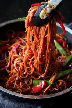 the noodles are being lifted with chopsticks from the skillet to be eaten