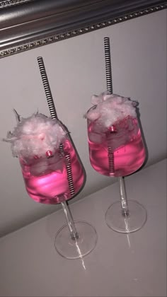 two wine glasses filled with pink liquid on top of a white counter next to a mirror