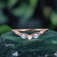 a rose gold ring with two pear shaped diamonds on top of a green leafy background