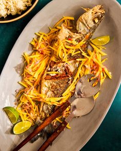 a white plate topped with fish covered in cheese next to rice and wooden spoons