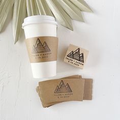 two coffee cups sitting next to each other on top of a white table with palm leaves