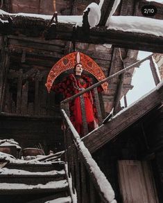 a woman in red is walking up some stairs with an orange umbrella and snow on the ground