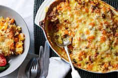 a casserole dish with cheese and vegetables next to a bowl of salad on a table