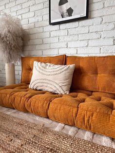 an orange couch sitting in front of a white brick wall