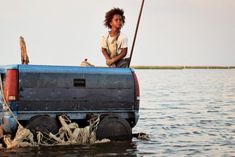 a boy is sitting on top of a truck in the water with a fishing pole