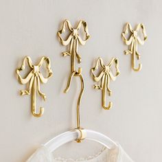 three pairs of gold metal clothes hangers on a white wall next to a lace shirt