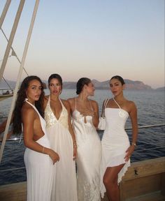 four beautiful women in white dresses posing for a photo on the deck of a boat