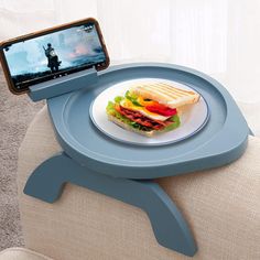 there is a plate with a sandwich on it and a cell phone in the holder