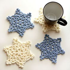 four crocheted snowflakes are next to a coffee cup