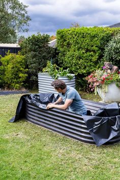 a man sitting on top of a black bench in the middle of a yard next to potted plants