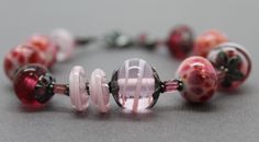 "In the mood for pink? Then this bracelet fits perfectly! It features a selection of my handmade pink lampwork beads. The colors range from dark translucent pink, pink and purple frit beads, to light pink swirls. These beads are simply stunning! Such a beautiful combination for Spring! The beads are strung along side sterling silver flower bead caps and pink Tourmaline rectangle shaped gemstone beads. I have made the lampwork beads in this bracelet. The sterling silver has been oxidized to add d Pink Czech Glass Beaded Bracelets With Colorful Beads, Handmade Pink Glass Bracelets, Adjustable Pink Multi-strand Beaded Bracelets, Adjustable Pink Glass Bracelets, Pink Beaded Bracelet, Pink Multi-strand Jewelry With Polished Beads, Pink Beaded Bracelets, Lampwork Jewelry, Pink Beaded