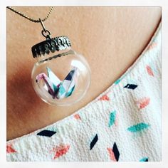 an origami crane in a glass ball on a woman's neck with a chain