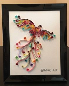 a colorful bird made out of paper in a black frame