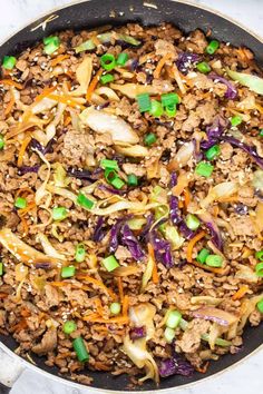 a skillet filled with ground beef, cabbage and carrots on top of a marble counter