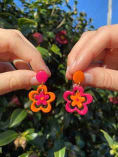 two hands are holding colorful flower shaped earrings