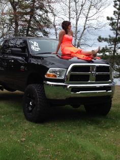 a woman in an orange dress sitting on the hood of a black dodge ram truck