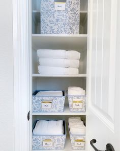 an organized closet with white linens and blue boxes on the bottom shelf in front of it