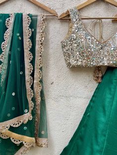 A three-piece emerald green mirror lehenga set from the Priti Sahni collection. This beautiful raw silk emerald green lehenga with a sari zari border detail is paired with a nude mirror blouse in pearl, and zardozi hand embroidery. This outfit is completed with an emerald green mirror work net dupatta with scalloped edging.