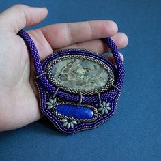 a hand holding a purple beaded brooch with a stone in it's center