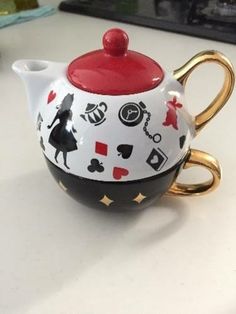 a ceramic teapot with a red lid and black design on it, sitting on a counter