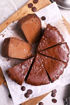 a chocolate cake cut into slices on top of a cutting board with chocolate chips around it