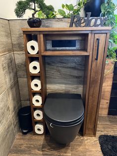 a black toilet sitting next to a wooden shelf with rolls of toilet paper on it