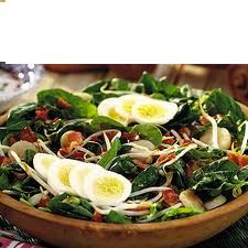 a salad with spinach, hard boiled eggs and bacon in a wooden bowl on a table