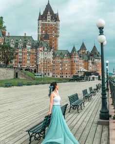 a woman in a long blue dress is standing on a boardwalk near benches and lamps