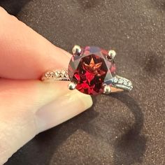 a woman's hand holding a ring with a red and white diamond in it