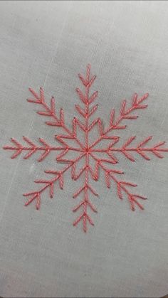 an embroidered snowflake is shown on a white piece of cloth with red thread