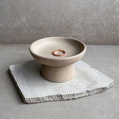 a small white bowl sitting on top of a stone slab with a ring in it