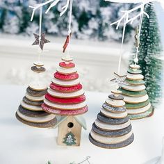 three wooden christmas trees hanging from strings on a white table with snow and evergreens in the background