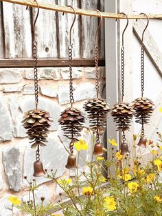 three metal bells hanging from chains in front of a stone wall with flowers and yellow daisies