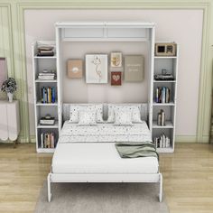 a white bed sitting next to a book shelf filled with books on top of a hard wood floor