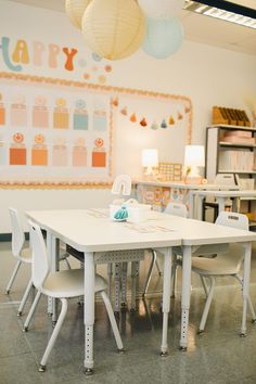 a white table and chairs in a room with paper lanterns hanging from the ceiling above it