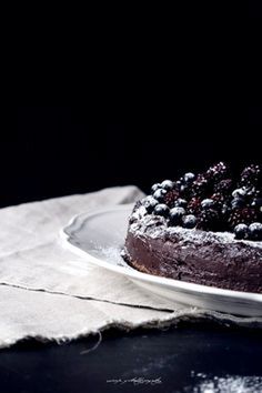 a chocolate cake sitting on top of a plate covered in powdered sugar and blueberries